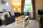 A wide view of the lounge, showing a fabric sofa with cushions and a white, wooden coffee table.
